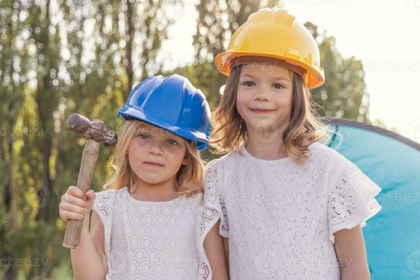 two little girls sisters pitching the tent at the campsite wearing protective helmets photo