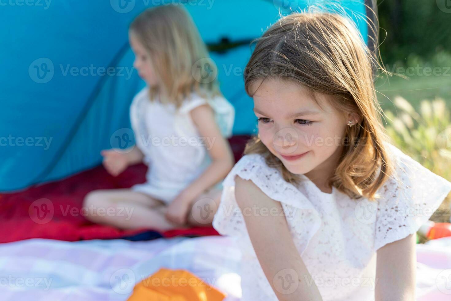 portrait of two blonde and pretty sisters sitting in a blue camping tent photo