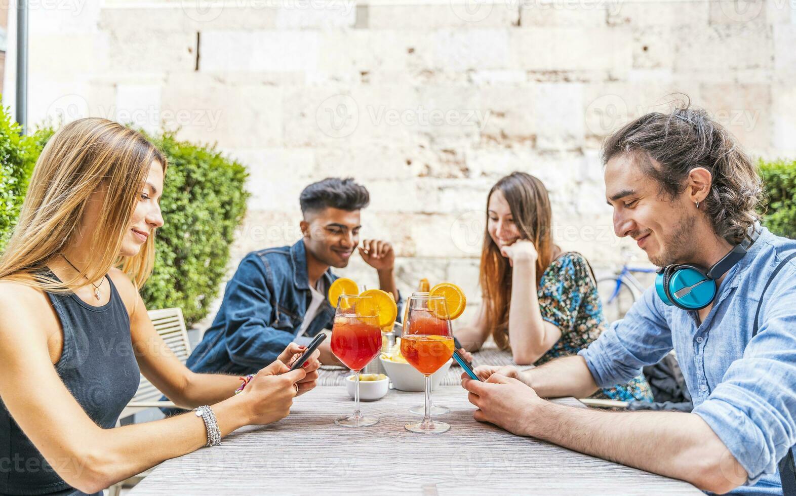 grupo de multirracial amigos sentado en un mesa al aire libre utilizando teléfonos inteligentes foto