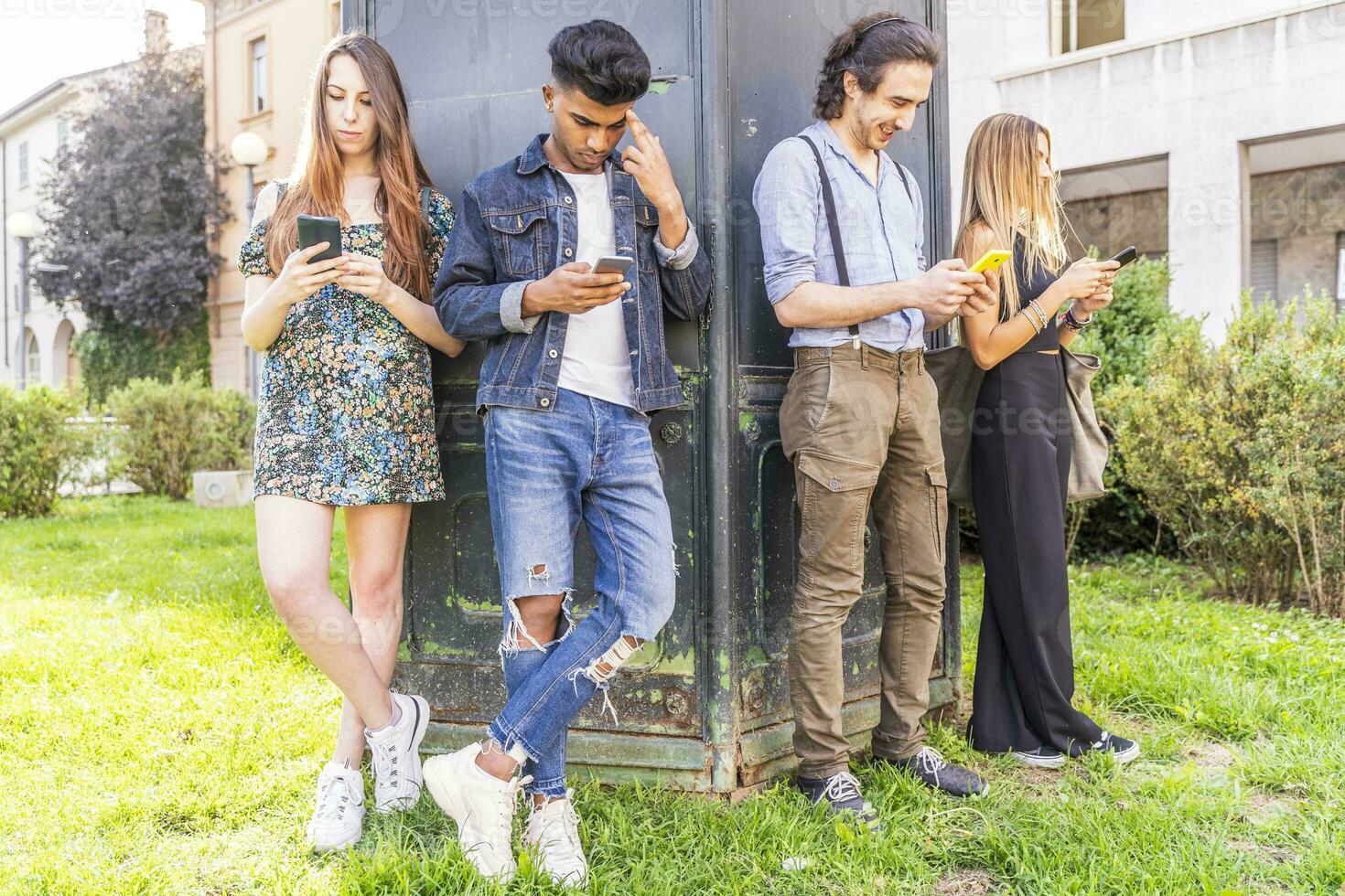 group of multiracial friends in front of a wall are using smartphones to share content photo