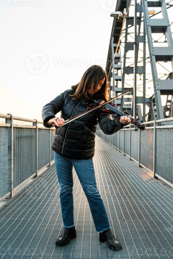 atractivo medio Envejecido mujer jugando un eléctrico violín al aire libre foto