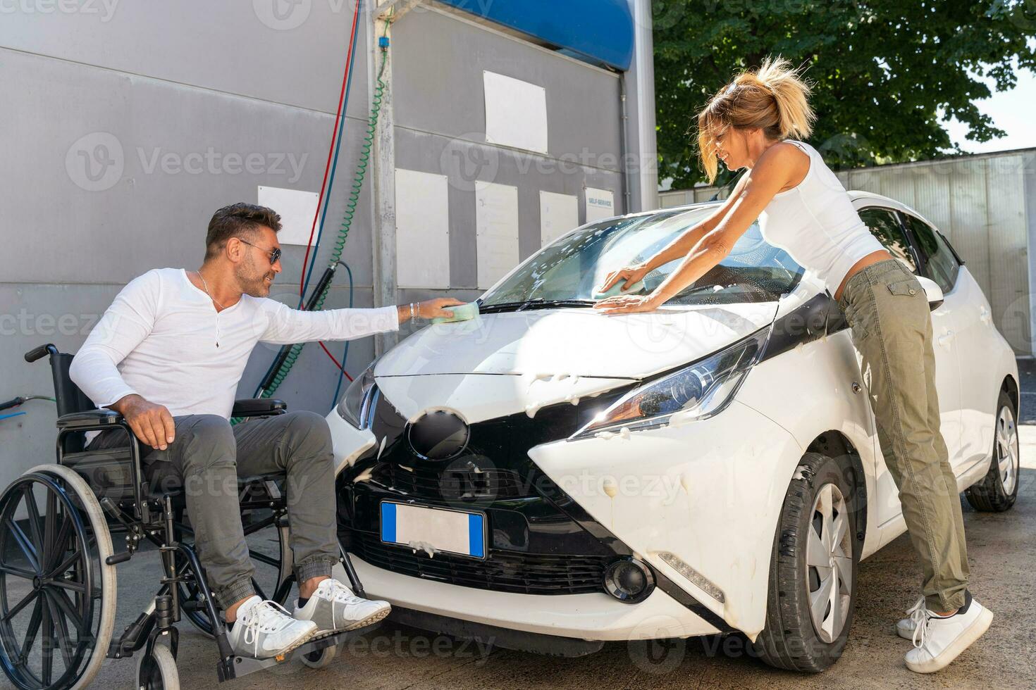 happy middle aged couple with man sitting on wheelchair washing car at public car wash photo