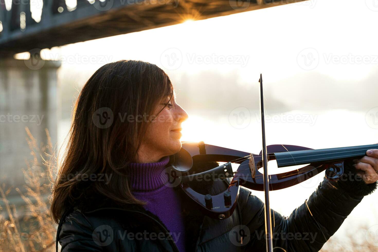 atractivo medio Envejecido mujer jugando un eléctrico violín al aire libre foto