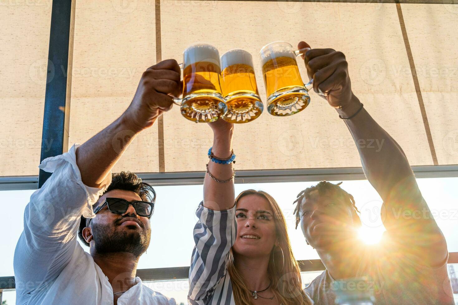 small group of young adult multiethnic friends toasting with three mugs of beer photo
