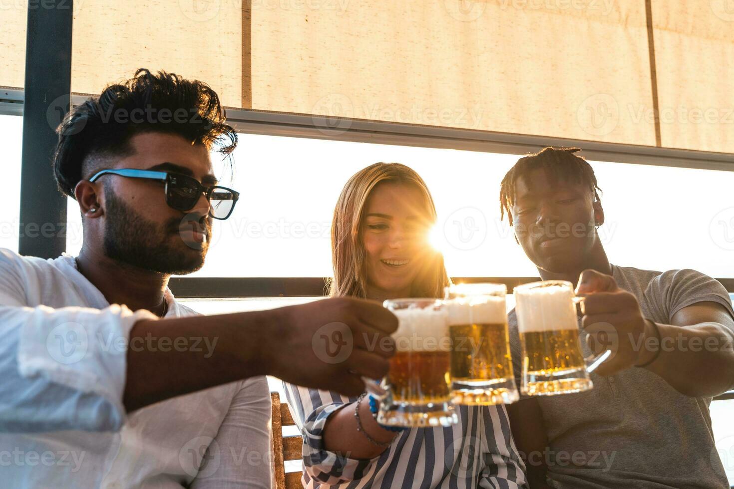 small group of young adult multiethnic friends toasting with three mugs of beer photo