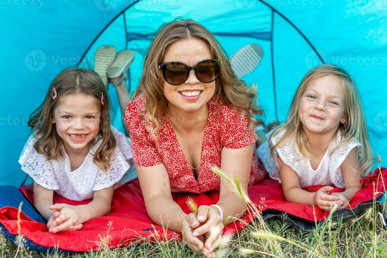 retrato de linda rubia mamá con su hijas acostado abajo en un azul cámping tienda foto