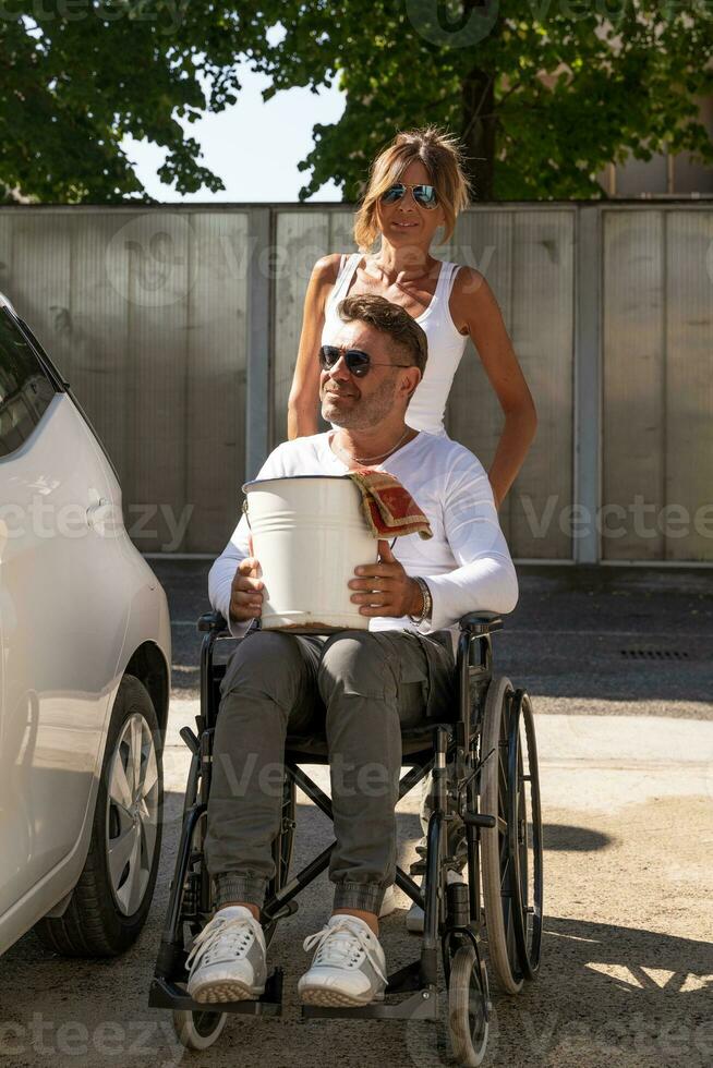 happy middle aged couple with man sitting on wheelchair washing car at public car wash photo