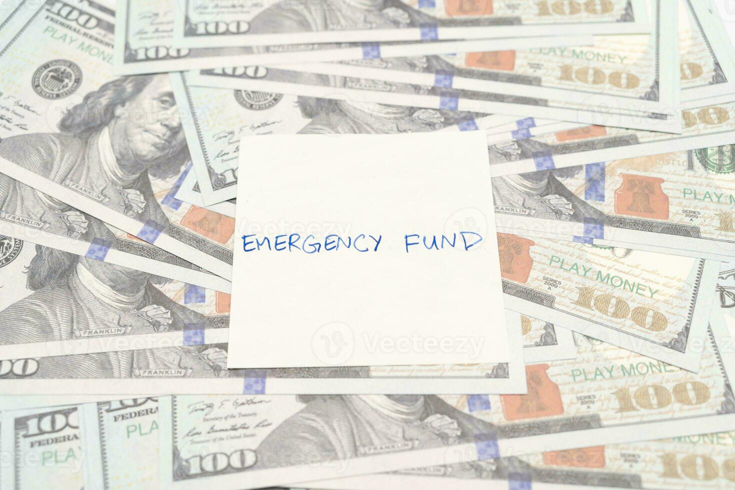 Paper note with phrase EMERGENCY FUND, dollar banknotes. Concept of money saving goal. Financial planning saving money for purpose of rainy day crisis. photo