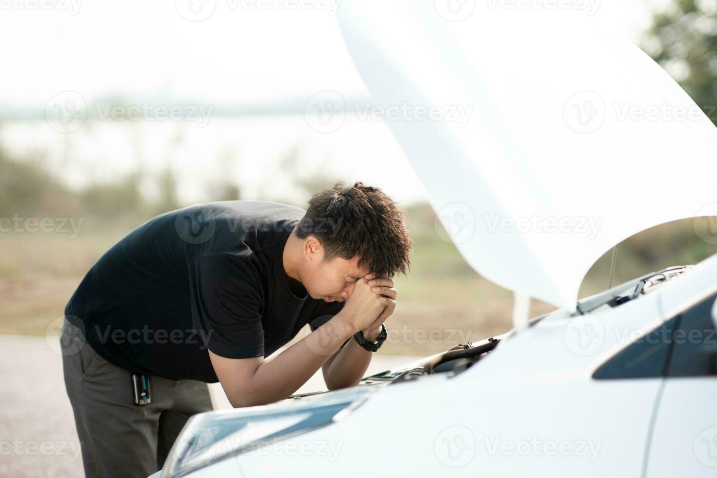 Worried asian young man stands in front of car checking condition after a broken car. Broken car down on the road. emergency service has broken car. photo