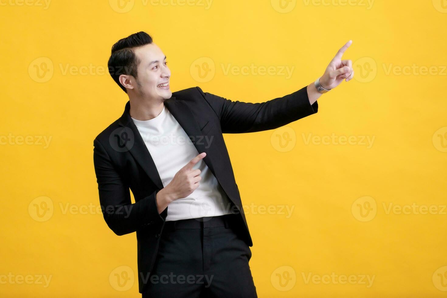 Portrait of happy young Asian man pointing fingers away at copy space isolated on yellow background photo