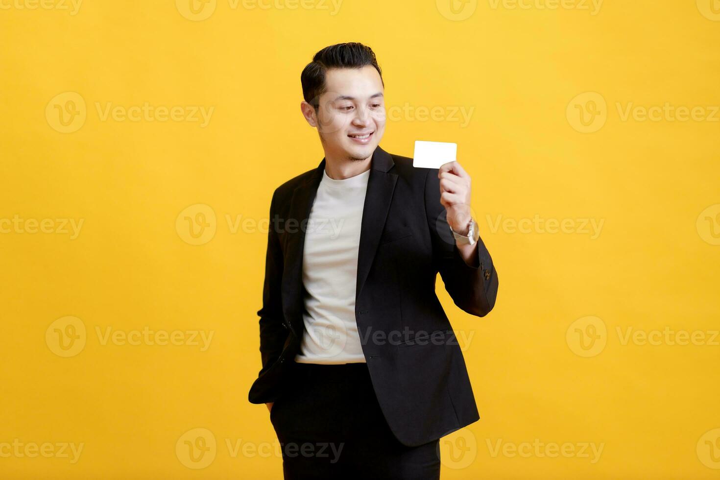 Young Asian man shows his credit card on a yellow background. photo