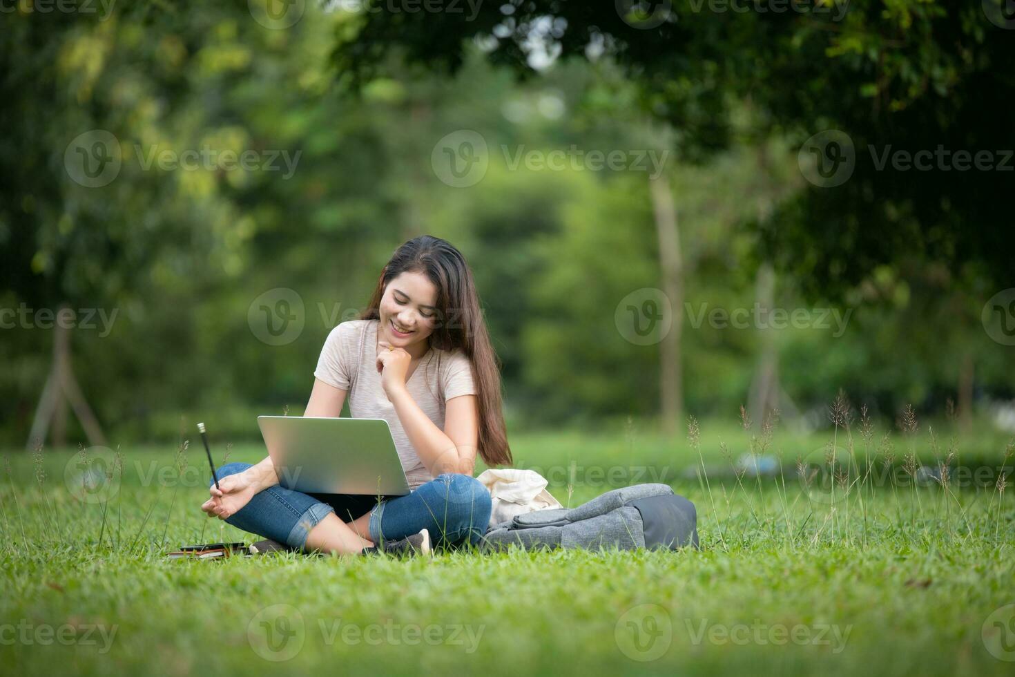 Confident smiling young Asian woman students reading and thinking doing homework with computer laptop on lawn in park. Concept of Education, Campus, teenage. photo