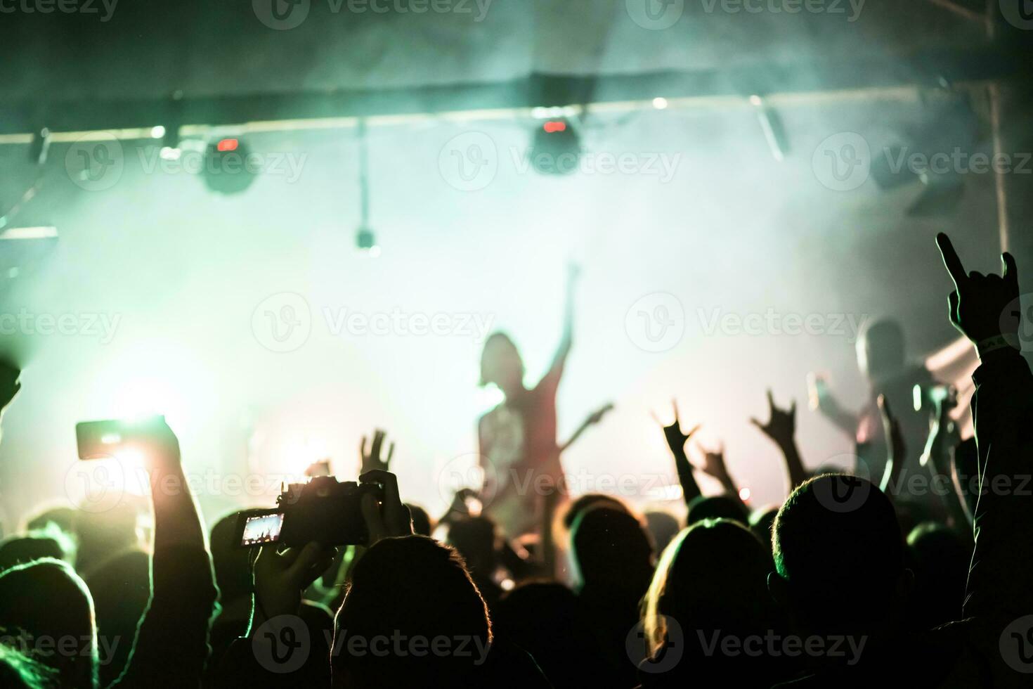 Crowd raising hands at the rock show. Audience in front of the stage. Live rock concert. Rock musicians on the stage photo