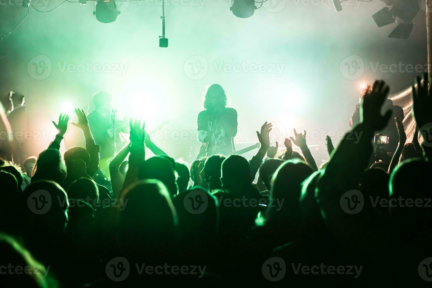 Crowd raising hands at the rock show. Audience in front of the stage. Live rock concert. Rock musicians on the stage photo