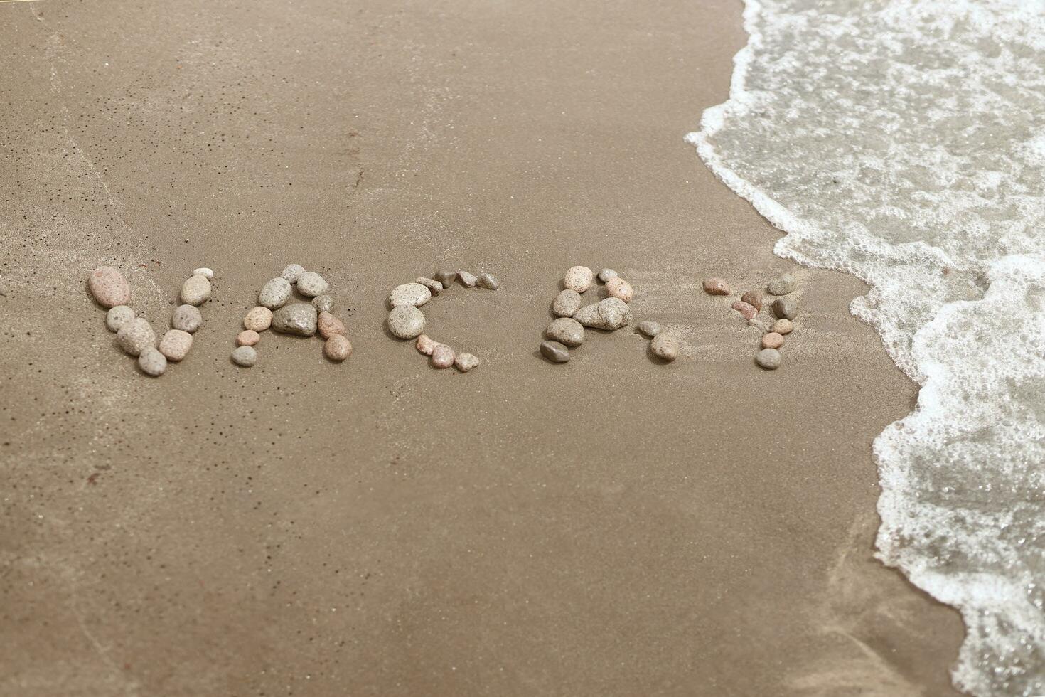 Word vacay written with pebble stones on the beach with a wave photo
