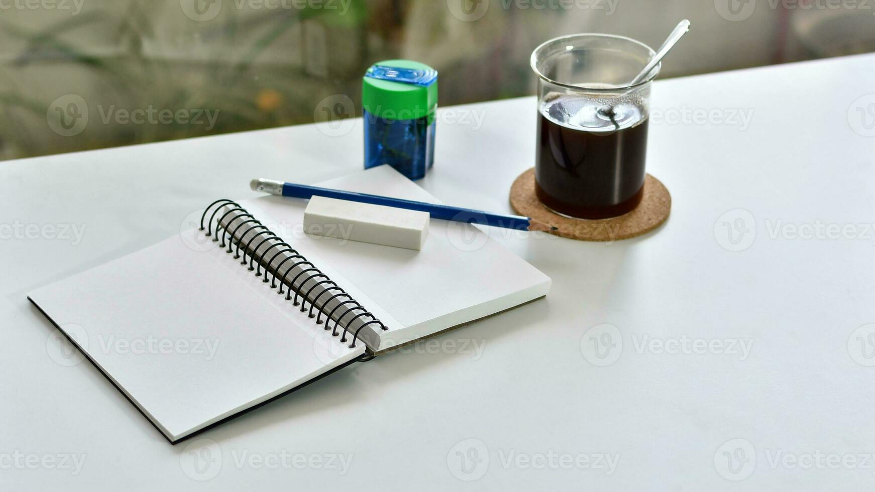 Desk with notebook, pencil, eraser and cup of coffee, next to a window. photo