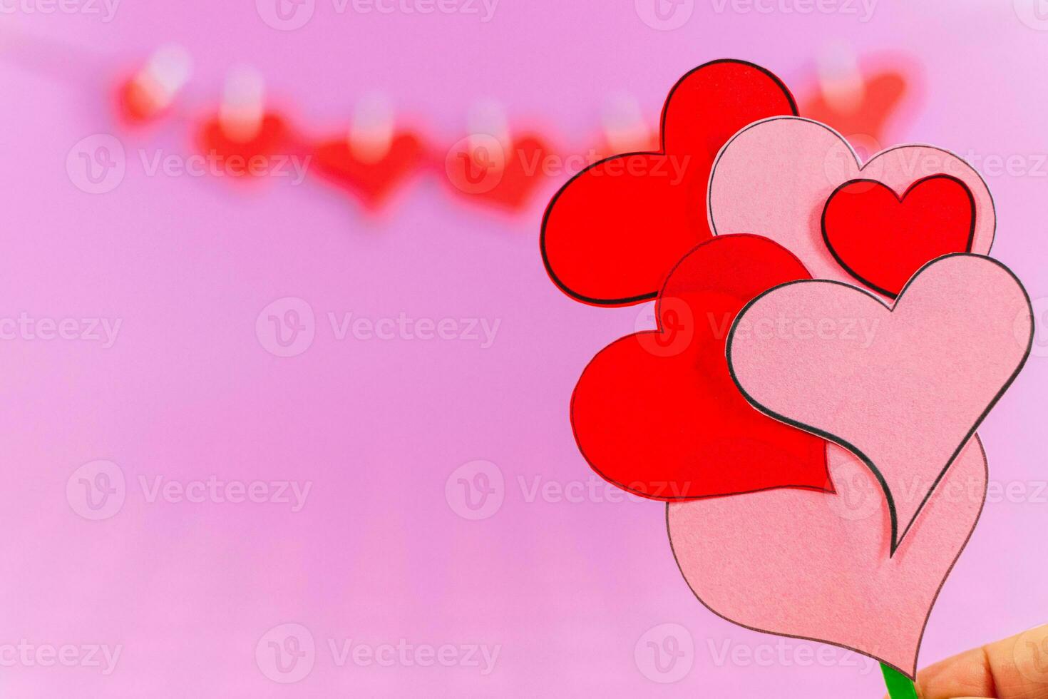 Red love hearts and female hand with bouquet of little hearts on pink background. photo