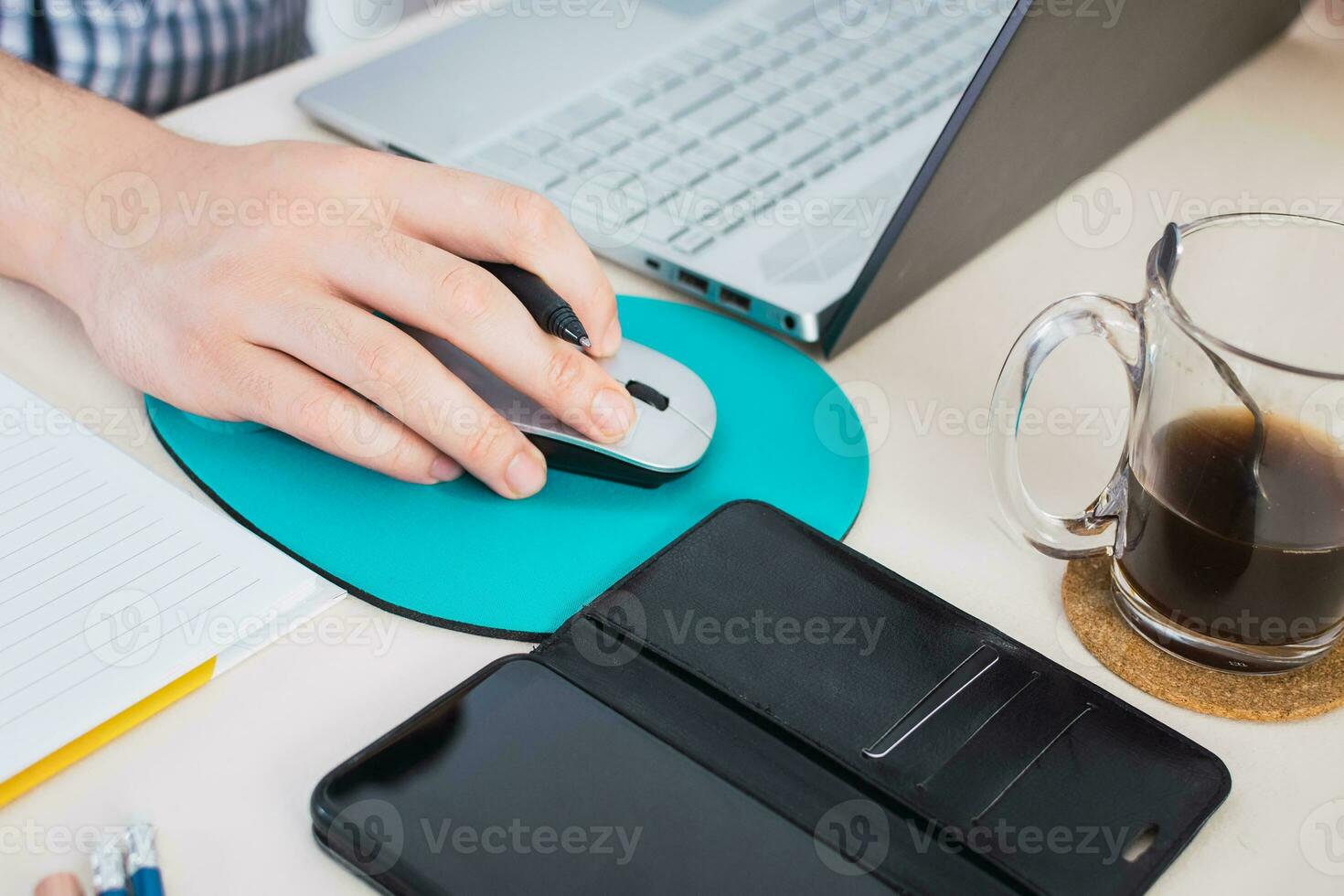 Businessman using computer mouse, laptop, cell phone, notebook and coffee cup on work desk. photo