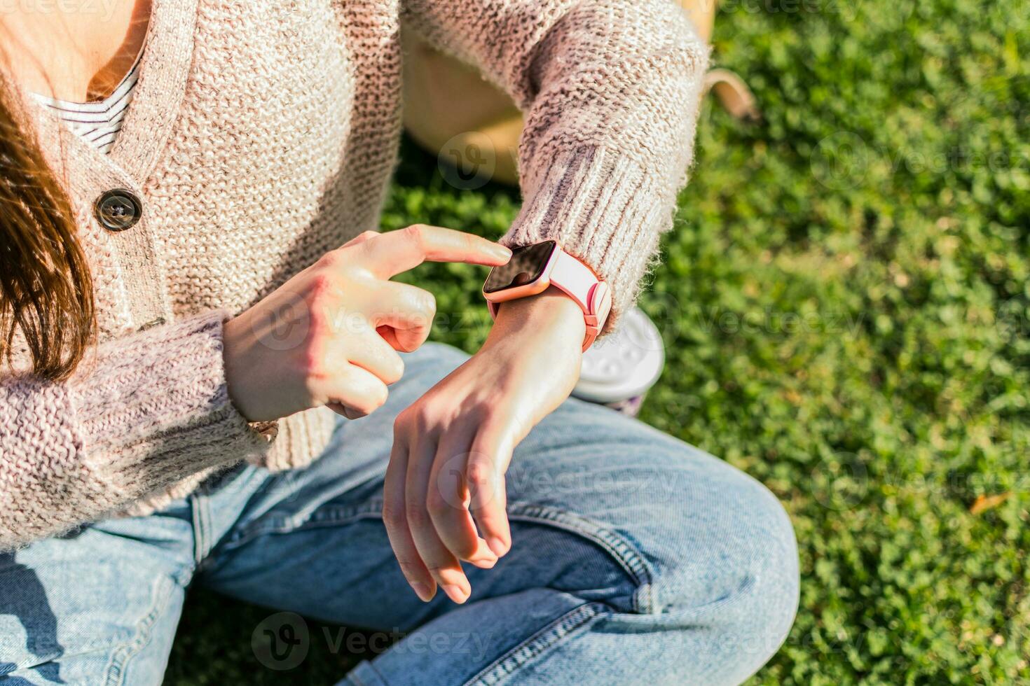 Close up of woman's hands checks the time on smart watch sitting in a park photo
