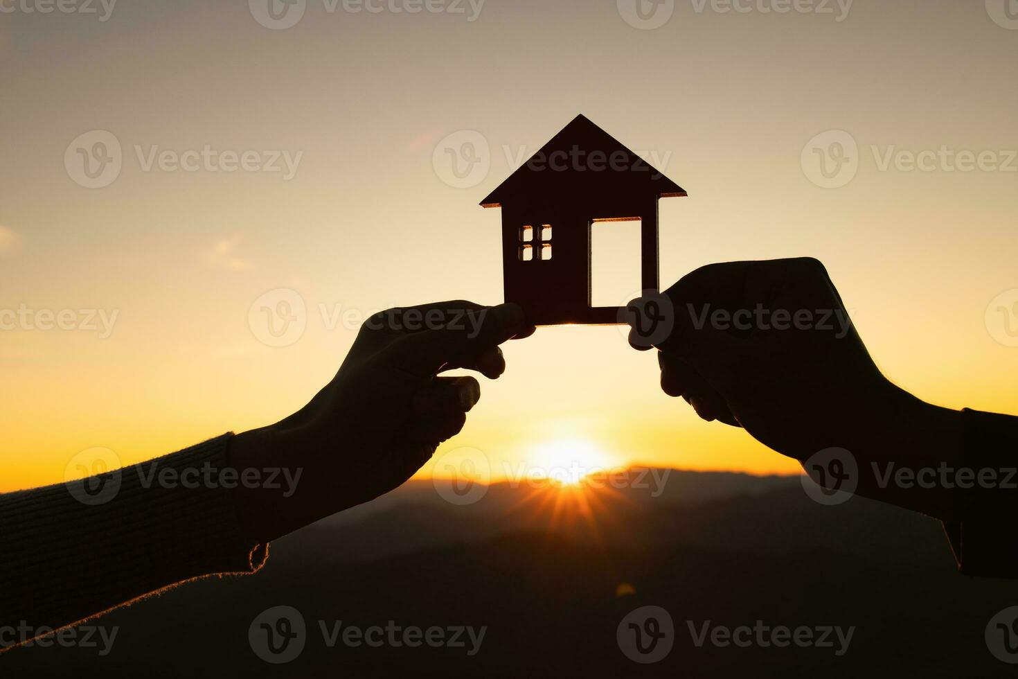 silhouette of male and female hands holding model house at sunset Concept of buying houses, real estate. photo