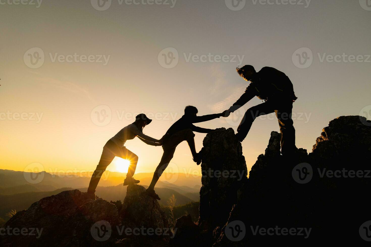 Silhouette of  Hikers climbing up mountain cliff. Climbing group helping each other while climbing up in sunset. Concept of help and teamwork. photo