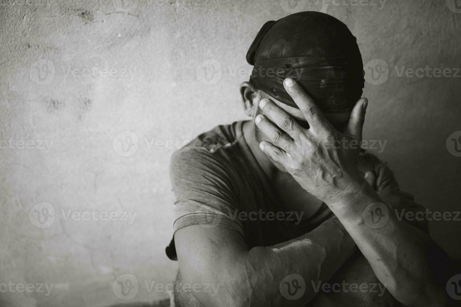 A drug addicted homeless man sitting alone and depressed in an abandoned house feeling anxious and lonely. photo