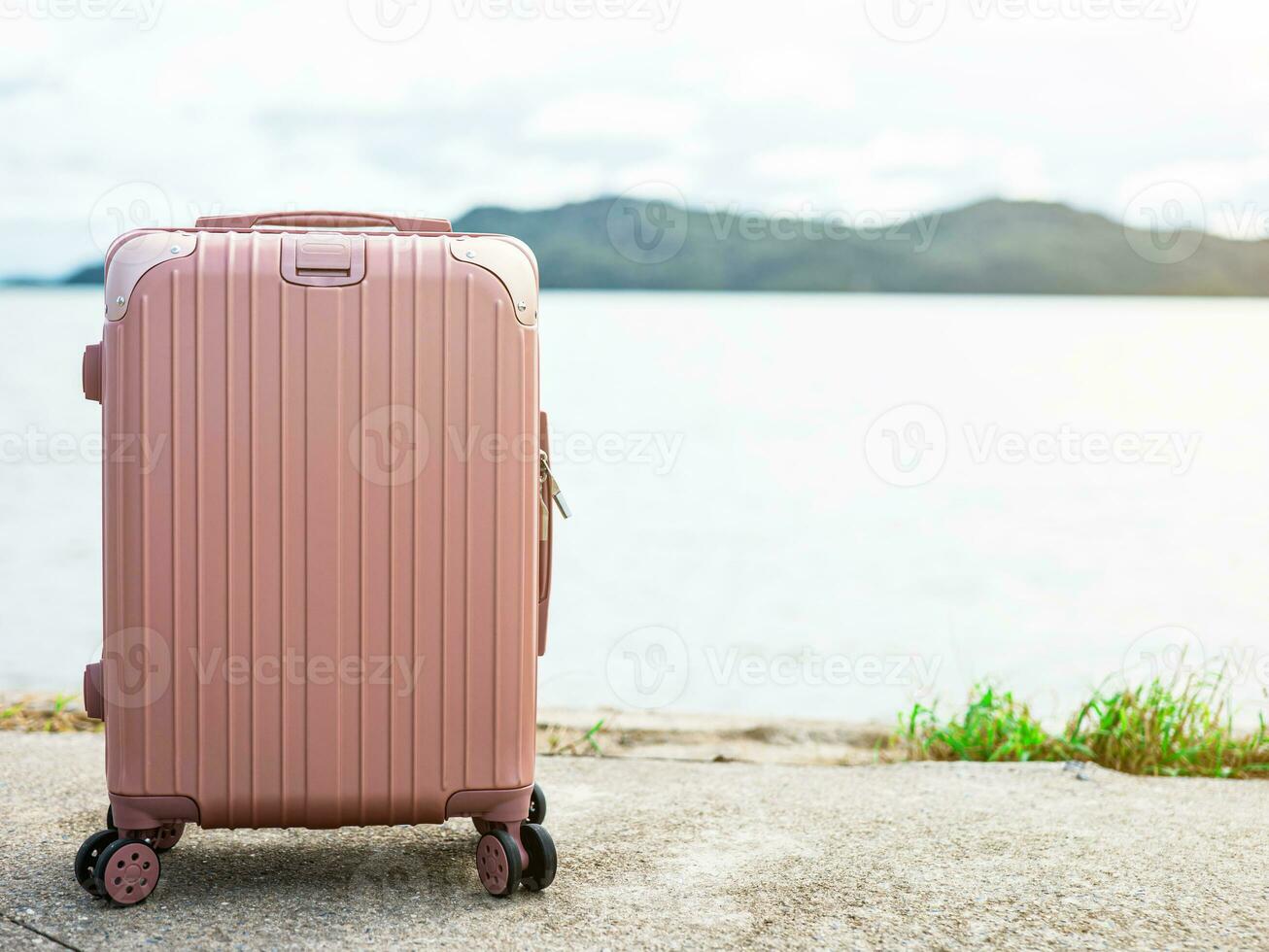 One pastel pink suitcase Laid out in the background is a blurred view of the sea on a sunny day. suitable for going on vacation photo