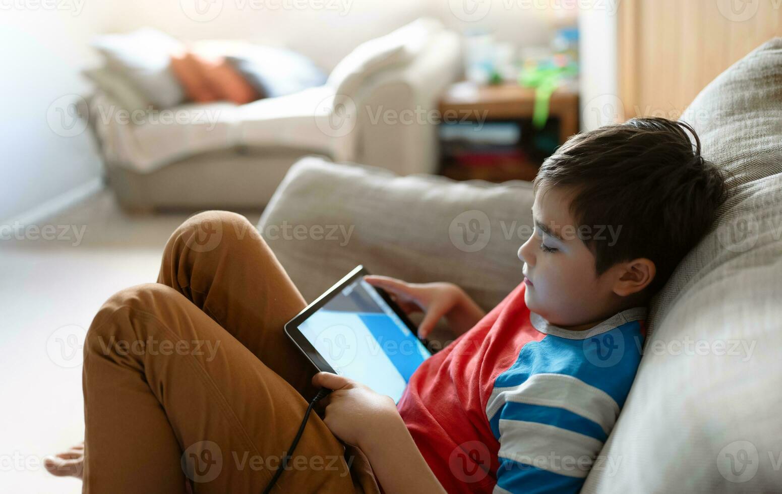 Preteen schoolboy doing homework with digital tablet in living room,Child using gadgets to study. Kid learns online from home,Education learning with new technology for kids. photo