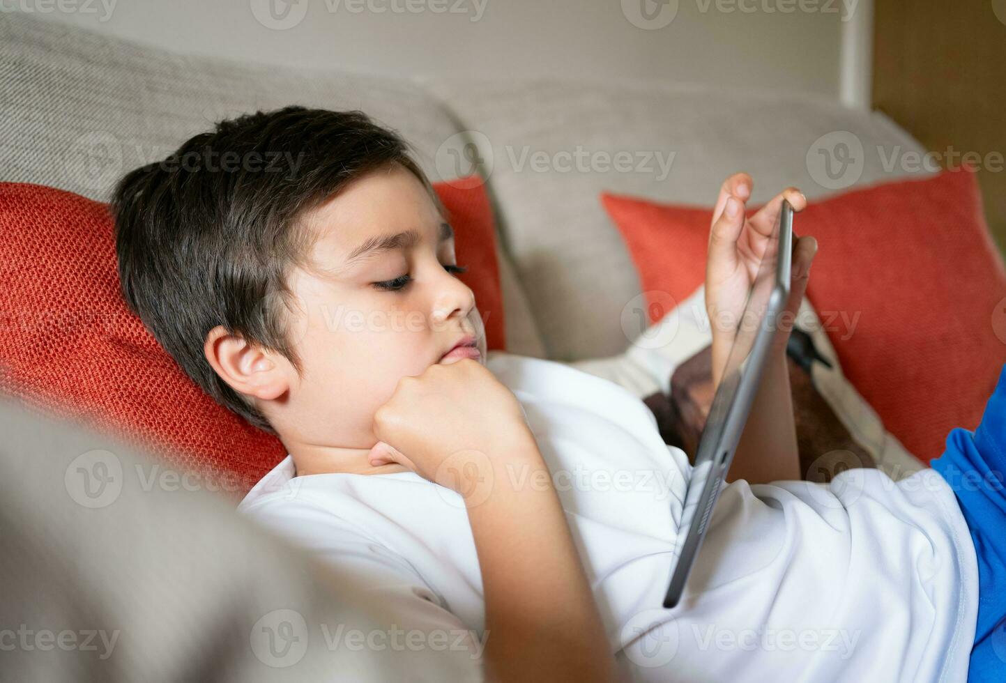 Kid doing homework with digital tablet in living room,Child using gadgets to study.School boylearns online from home,Education learning with new technology for kids. photo