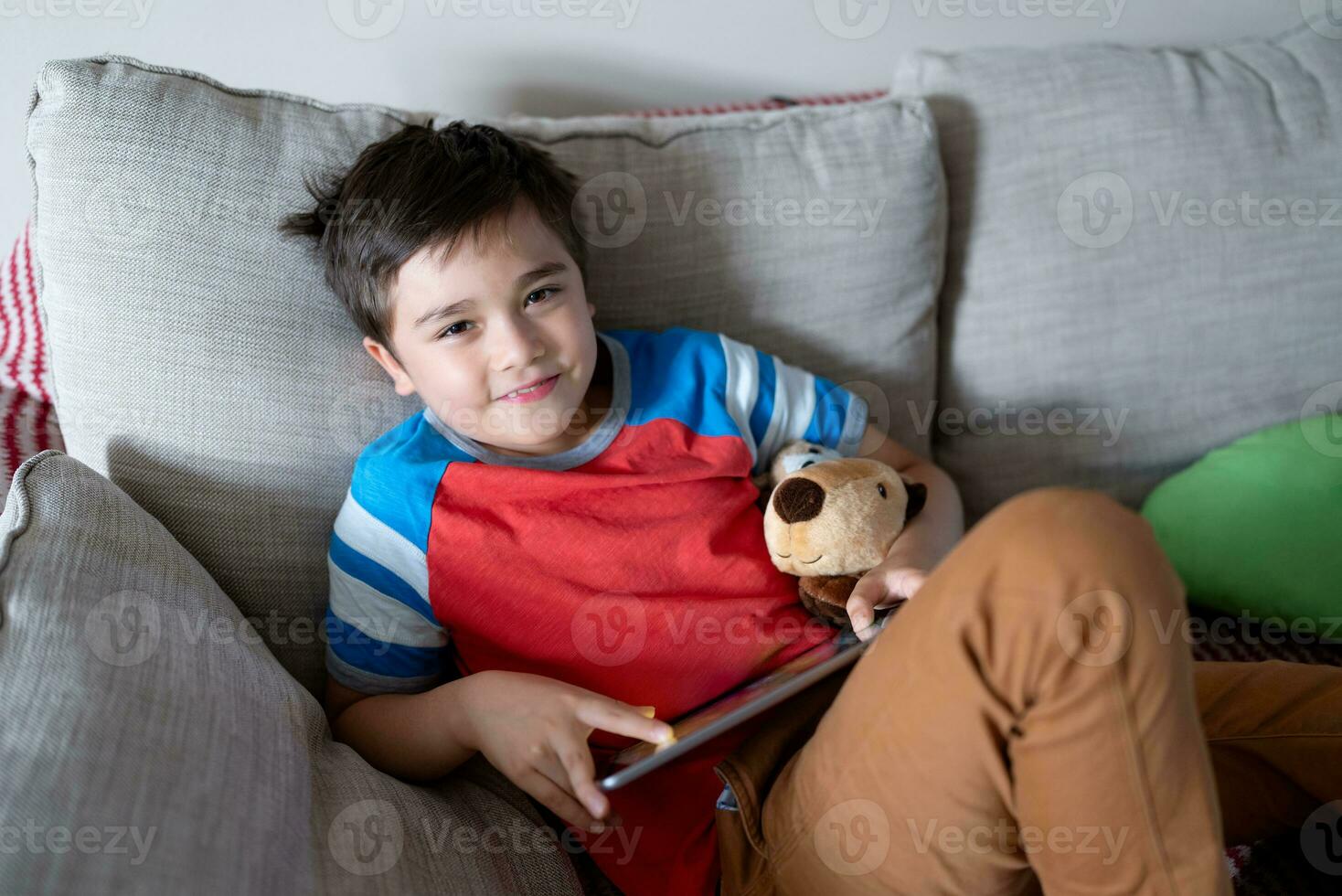 Preteen schoolboy doing homework with digital tablet in living room,Child using gadgets to study. Kid learns online from home,Education learning with new technology for kids. photo