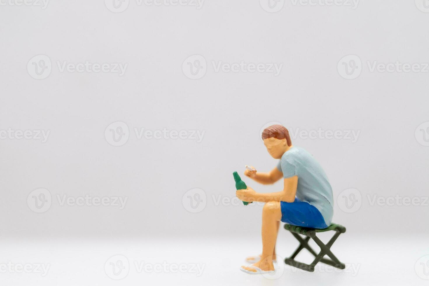 Miniature people Young man sitting on a lawn chair while clutching a water bottle. photo