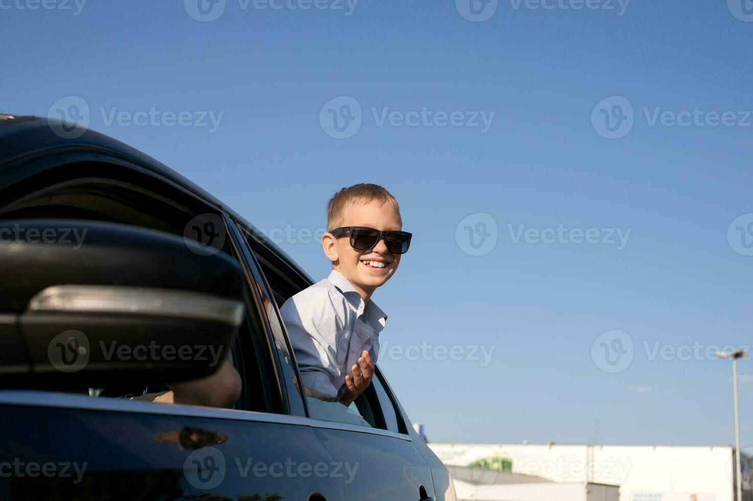 A cute boy in sunglasses looked out of the car window with a laugh.  photo