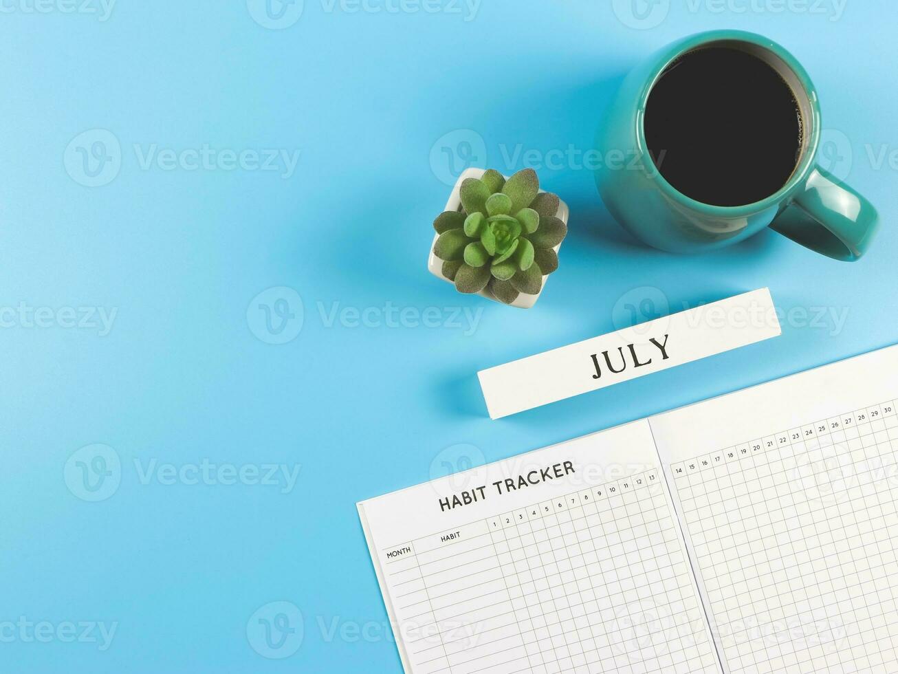 flat lay of habit tracker book with  wooden calendar december, blue  cup of black coffee and succulent plant pot on blue background with copy space. photo