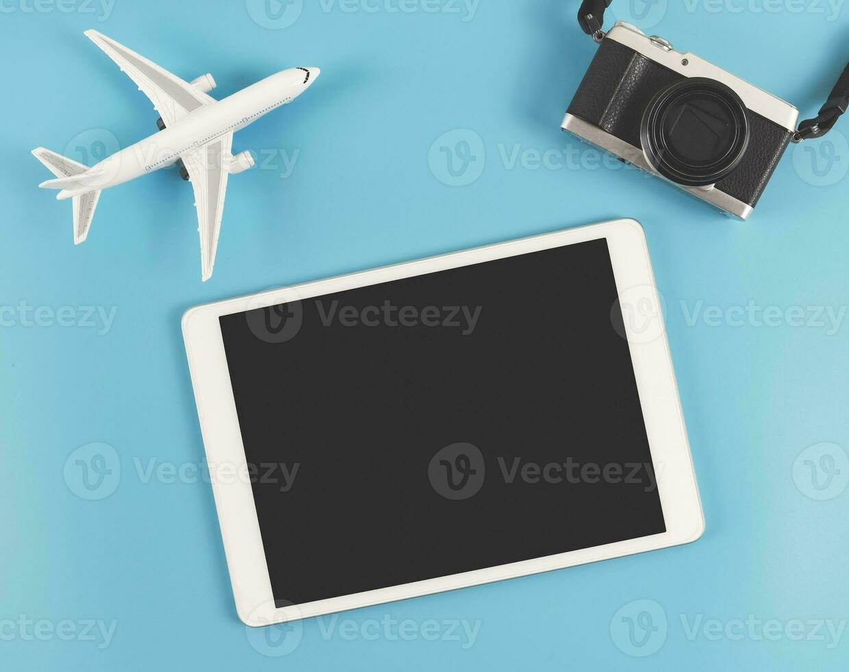 plano laico de digital tableta con blanco negro pantalla, digital cámara y avión modelo aislado en azul antecedentes. viaje planificación concepto. foto