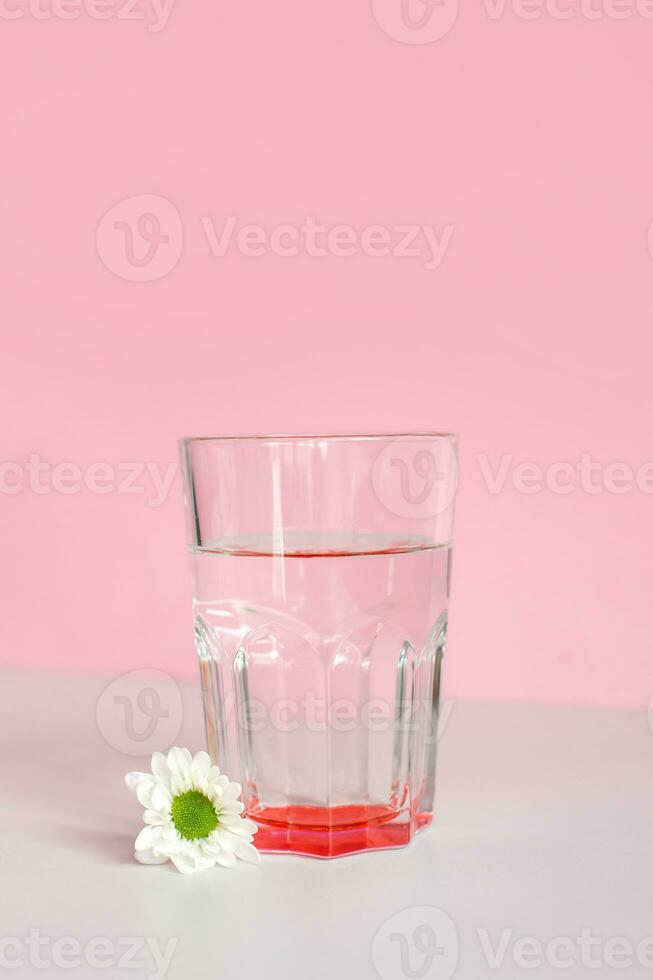 un vaso vaso con agua soportes en un rosado antecedentes con blanco crisantemo flores en el Mañana foto