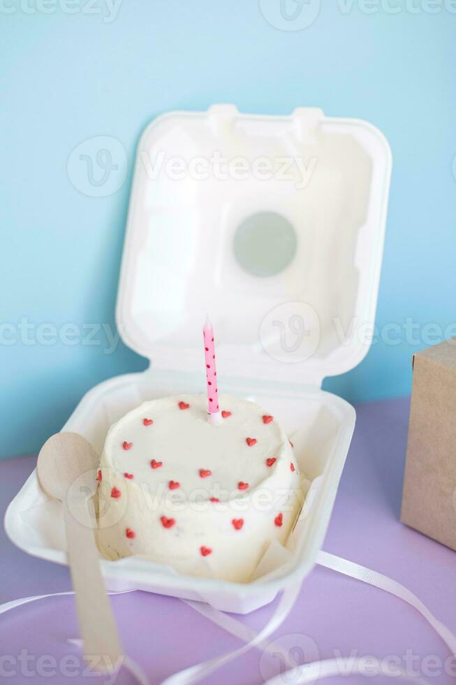A small bento cake in eco-packaging with a wooden spoon on a purple background without text photo