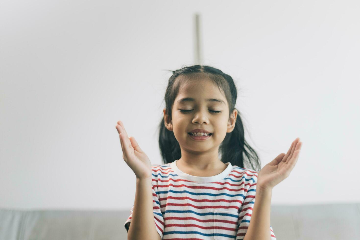 contento asiático niño niña meditando a hogar. niño sentado en sofá en vivo habitación y sonriente. foto