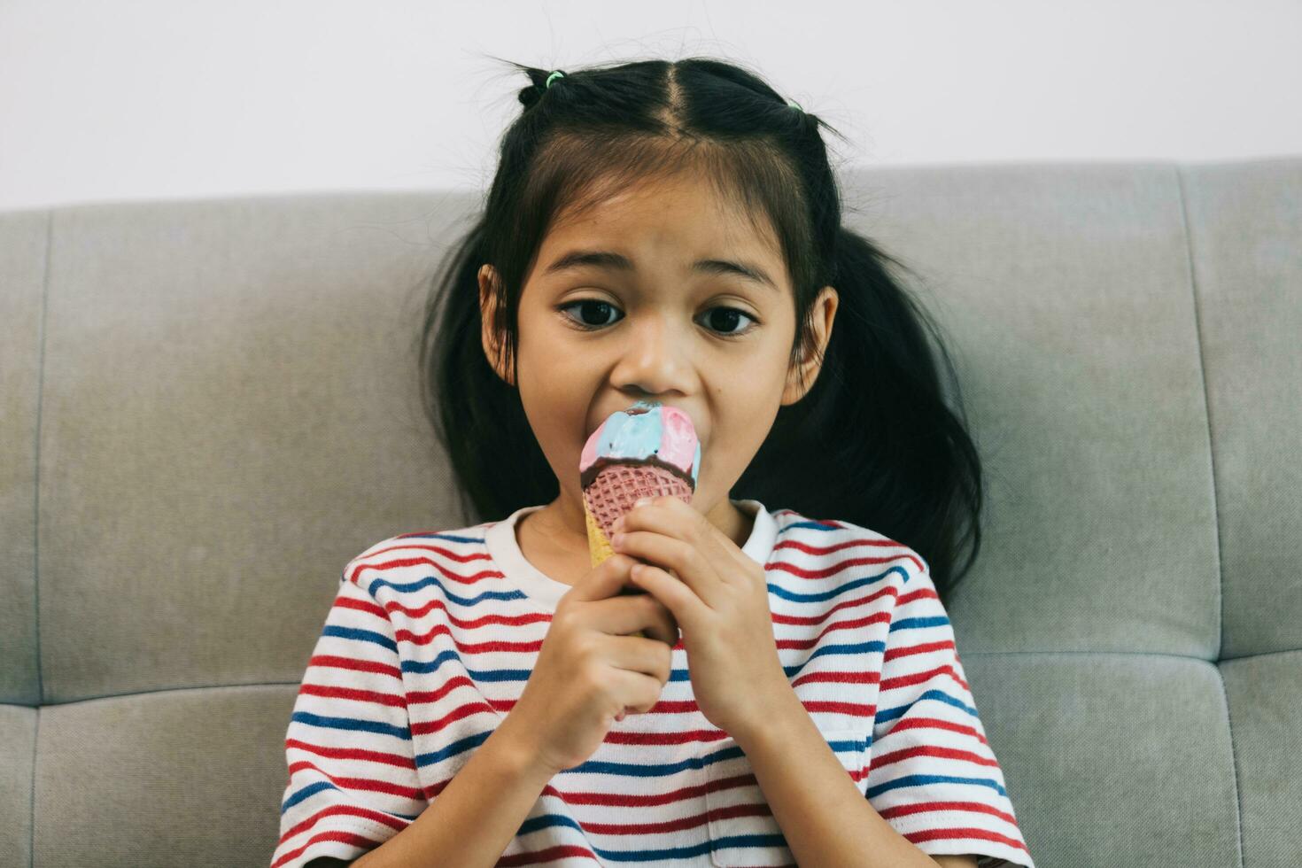 Cute little girl eating ice cream while sitting on sofa at home