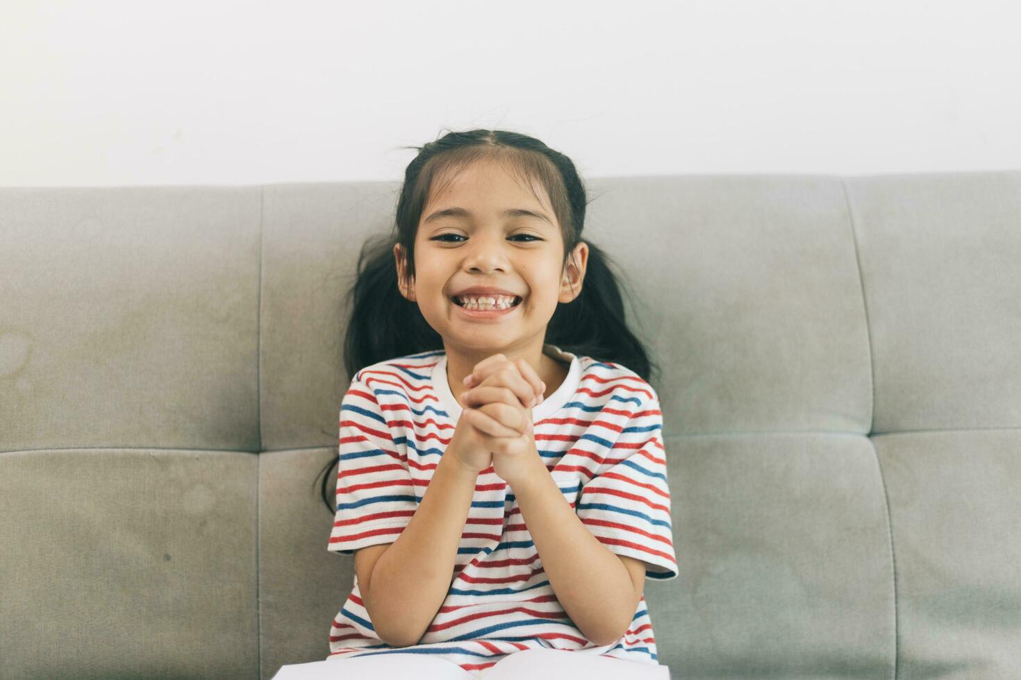 linda asiático niño niña sentado en sofá a hogar y sonriente foto
