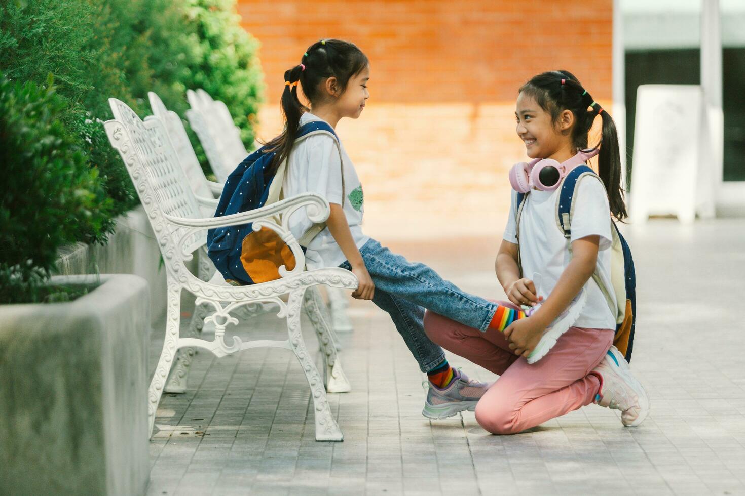 dos pequeño muchachas sentado en un banco en el parque y hablando. foto