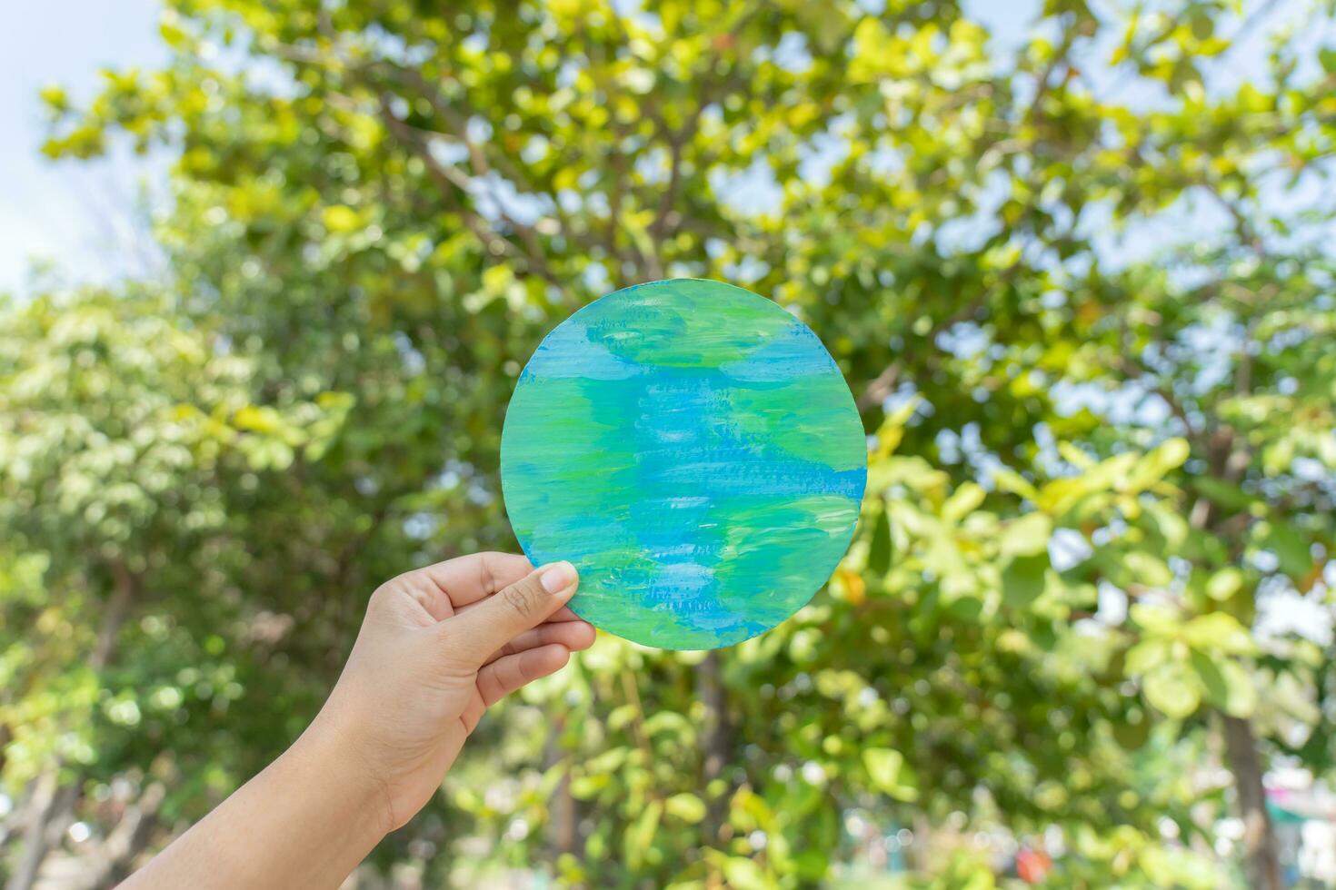 Hand holding earth sign up with natural environment sky and tree as background. Environment protection concept using paper cut planet earth symbol. photo