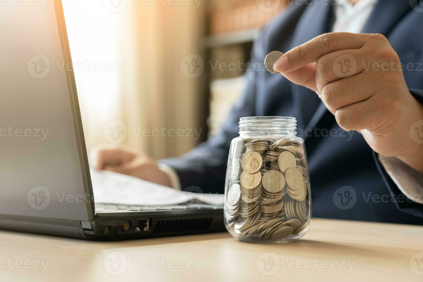 Business man working with laptop savings money Thai currency coins in jar for new house. Save money to rent or buy new living place. photo