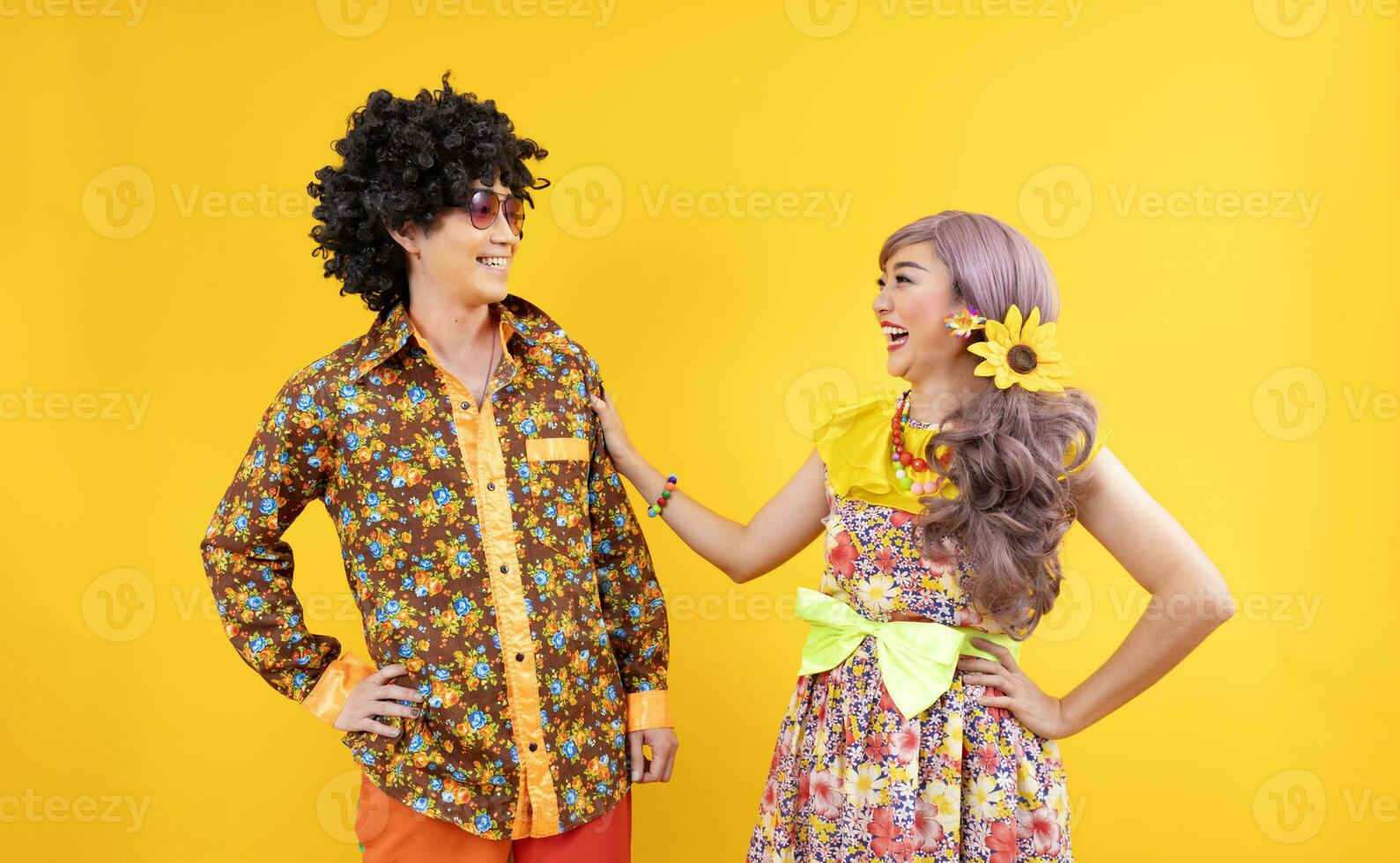 Asian hippie couple dress in 80s vintage fashion with colorful retro clothing while dancing together isolated on yellow background for fancy outfit party and pop culture photo