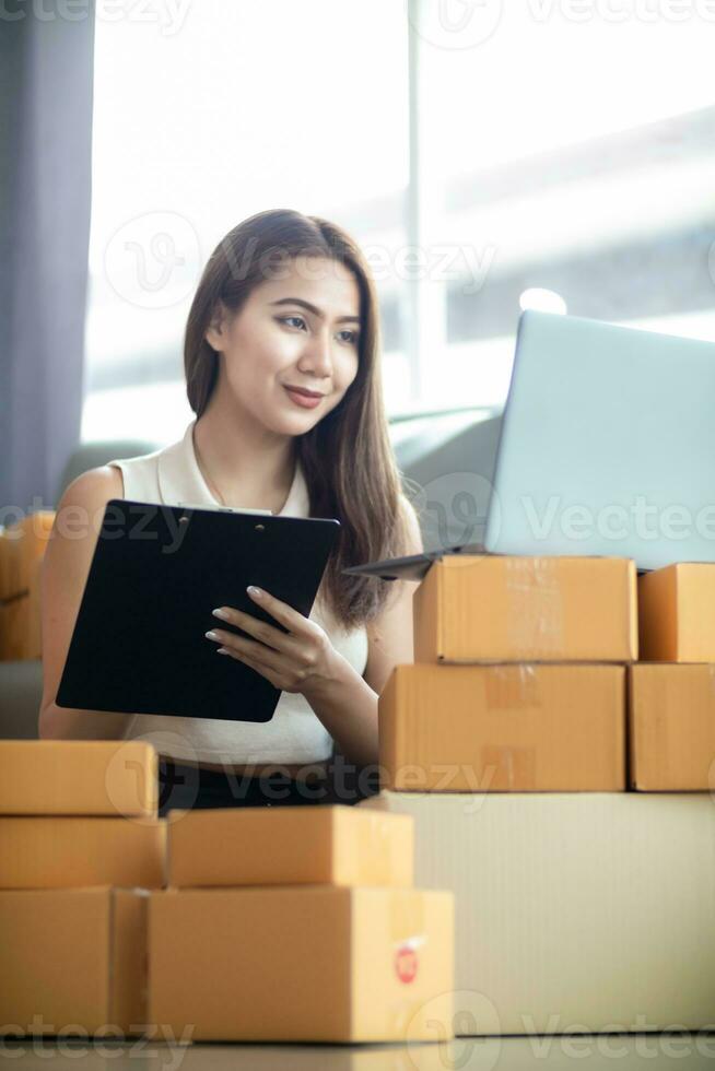 mujer comprobación paquete de bienes desde cliente en línea orden es solo en su hogar oficina como ella es un SME empresario y usos su teléfono y tableta a mercado en línea. concepto en línea ventas negocio foto