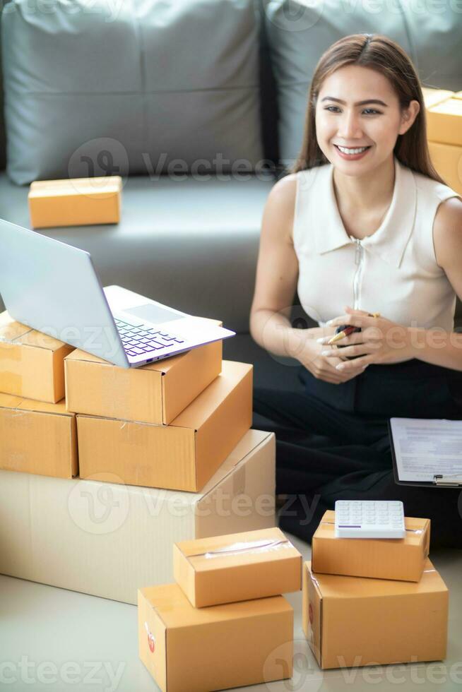 mujer comprobación paquete de bienes desde cliente en línea orden es solo en su hogar oficina como ella es un SME empresario y usos su teléfono y tableta a mercado en línea. concepto en línea ventas negocio foto