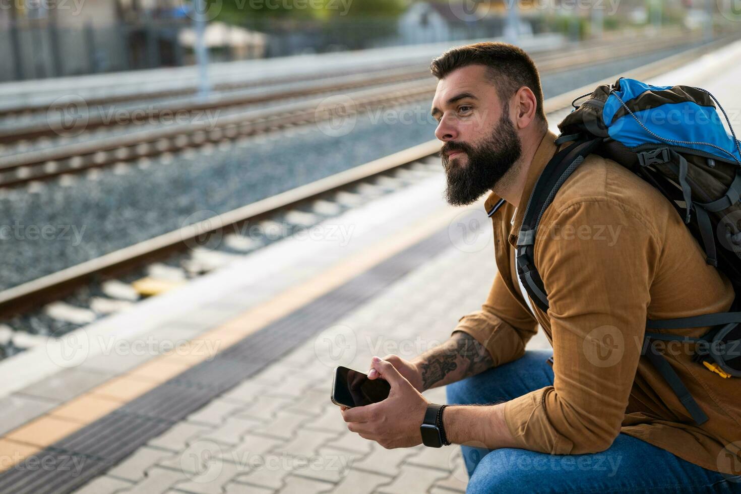 Adult man is sitting at railway station and waiting for arrival of train. photo