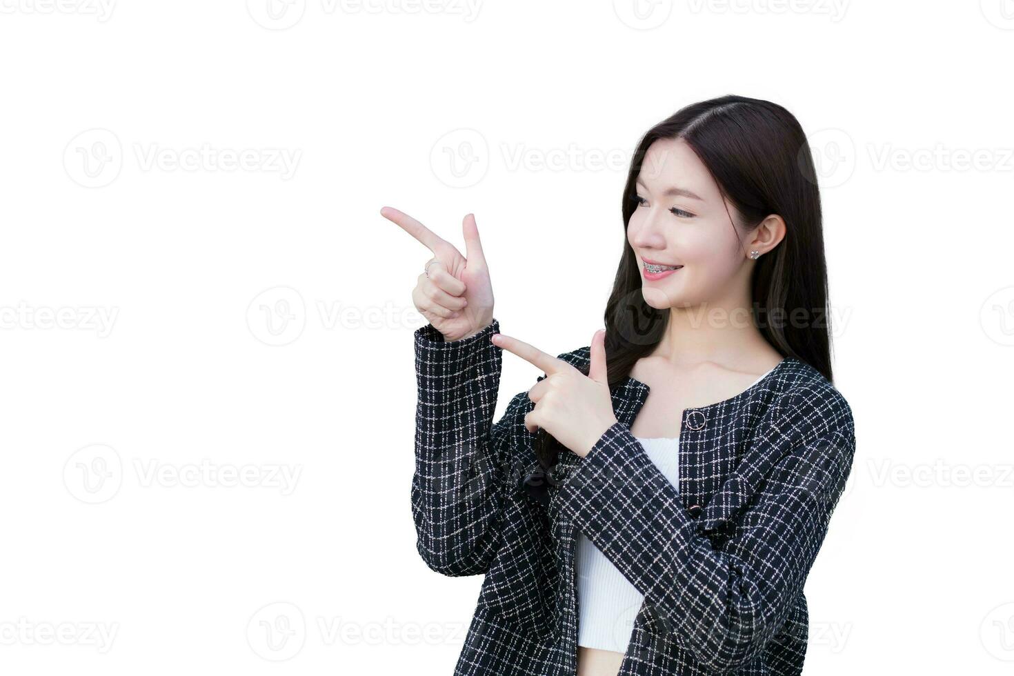 Asian professional working woman who wears black suit with braces on teeth is pointing hand to present something while isolated on white background. photo