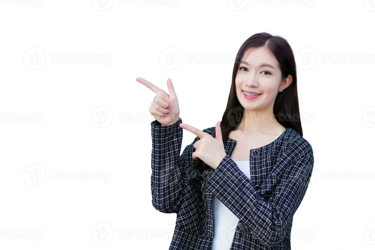 Portrait of Pretty long haired young Asian business woman in black suit with braces on teeth is pointing hand to present something with confidence while isolated on white background. photo