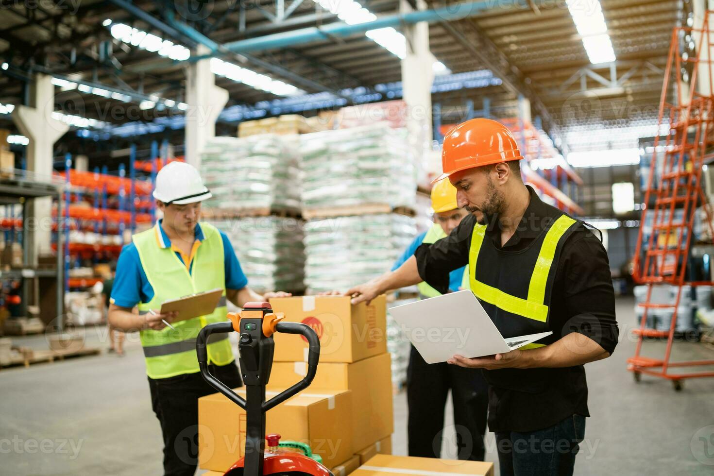Manager man using laptop check stock and control work with co-worker point at warehouse. Worker wearing high visibility clothing and hard hat, helmet to checking count up goods or boxes for delivery. photo