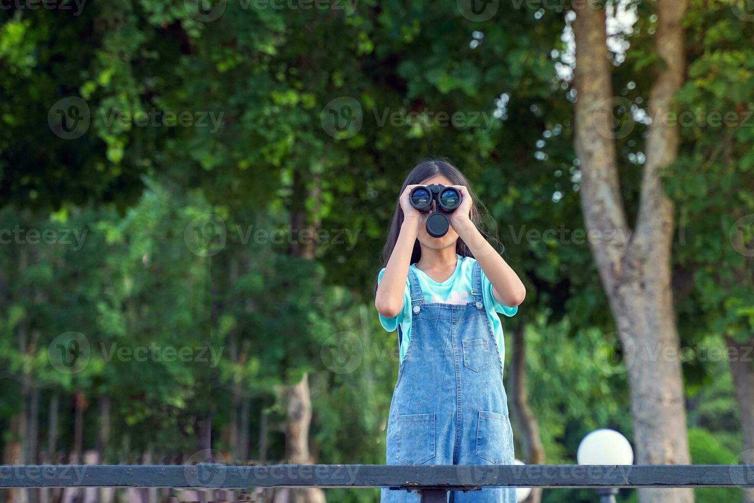 Asian girl uses binoculars to observe the nature, birds, and animals of the National Park while camping with her family. with the concept of learning outside the classroom nature study, exploration. photo